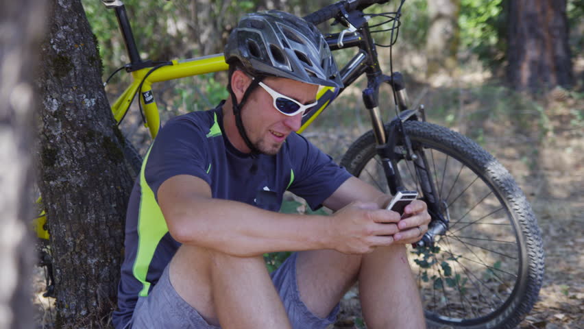 Man with mountain bike sits down taking break and checking cell phone