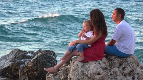 Family sitting on seashore cliff admiring nature, waves splashing on rocks