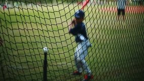 Shot from behind net of a Kid Practicing his Batting on a Baseball Field