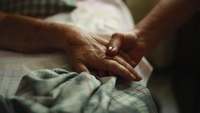 Pan of Unrecognizable Elderly person holding hands with another person to the bed where she is lying down