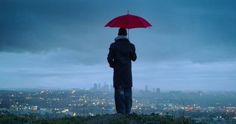 Man under red umbrella overlooking cloudy Los Angeles cityscape from Hollywood Hills at twilight. 4K UHD. Video Stok