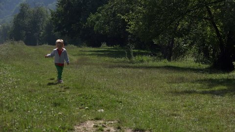 Lovely blonde boy running on green meadow