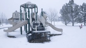 Playground surrounded by pine trees under snow at park during winter season.