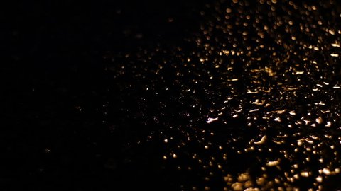 Variation of raindrops collecting in puddle lit by amber lighting.