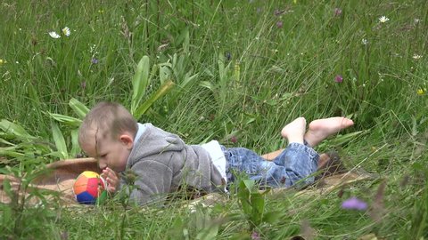 Little child lie down on green field barefoot
