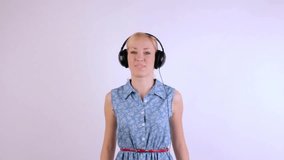 Young blonde girl with headphones on her head dancing while listening to music, in the end makes a kiss at the camera