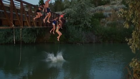 Group Of Wild Teens Jump Off A Bridge Into Water Below At Dusk In The Utah Desert