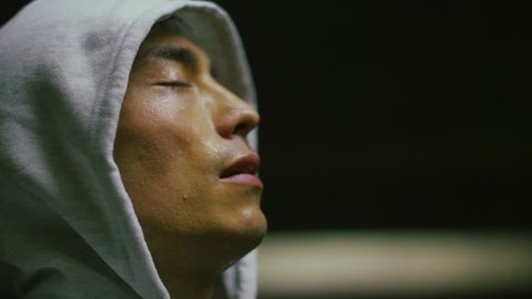 4K Hooded athlete breathing heavily and tilting his head to the light as he regains his breath in slow motion, shot on RED EPIC