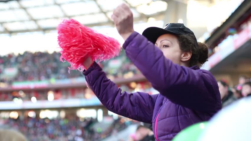 Woman in black cap shouts with red pompoms during football match at stadium
