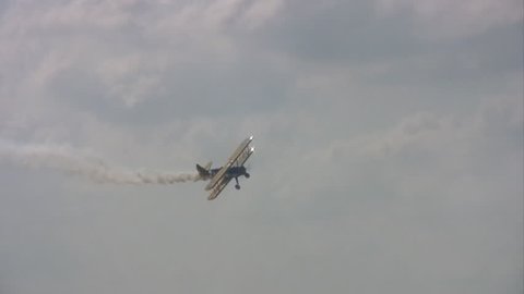 Video of an old WW I bi-plane flying in an airshow at Randolph AFB Texas. Smoke trailing the aircraft. Maneuvers and acrobatic flight. Skillful pilot gives thrill to spectators