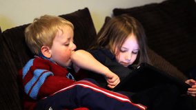 Two children play on a tablet together at home
