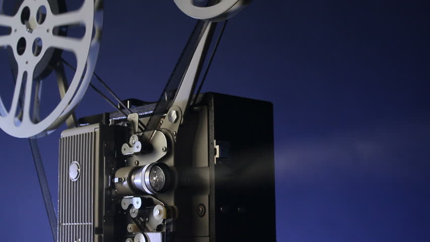 A motion picture movie projector sends a beam of light into the dark