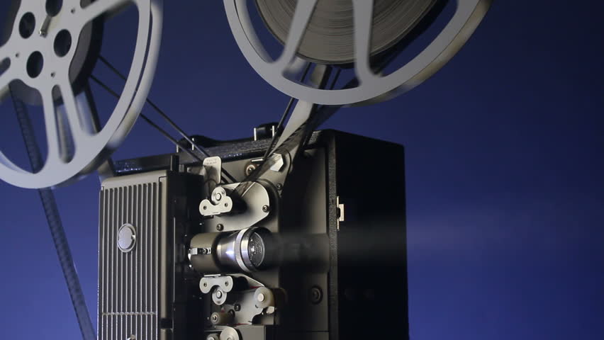 A motion picture movie projector sends a beam of light into the dark