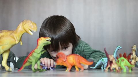 Adorable little boy, playing with plastic animals and dinosaurs on the floor
