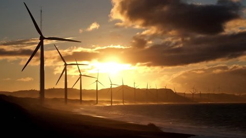 Wind turbine power generators silhouettes at stormy ocean coastline at sunset. Alternative renewable energy production in Philippines