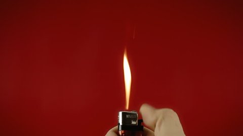 Frantically operating a cigarette lighter. Colorful close-up shot on red background.
