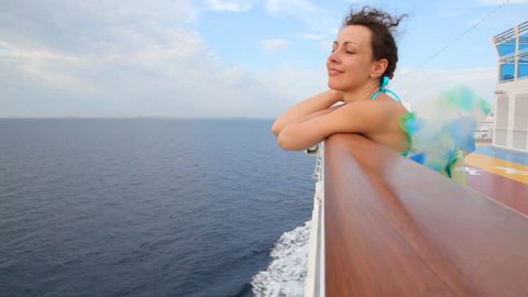 happy woman stands on deck of cruise ship, hair blowing in the wind