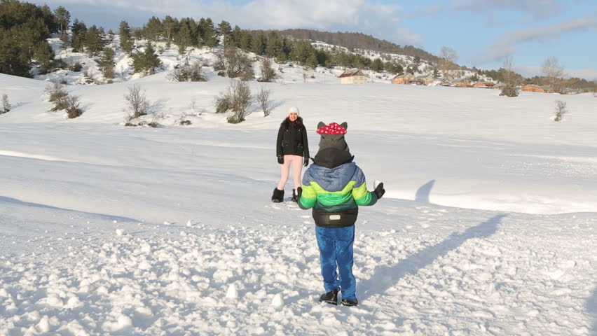 Happy woman and child playing with snow in winter park.