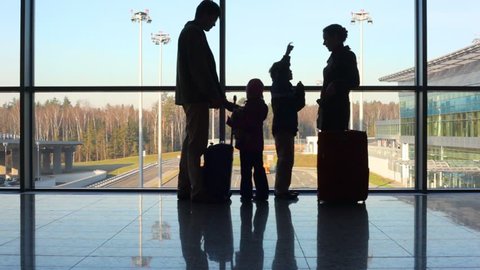 family of four stands against window at airport, then walks off