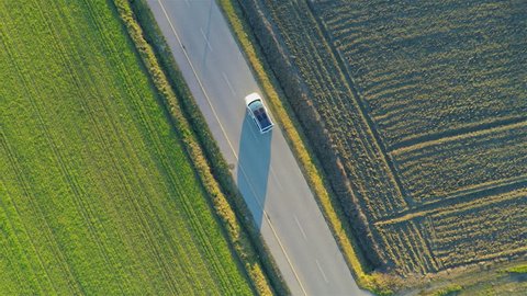 Flying vertically above car driving on road 4K. Aerial shot from top of car vehicle driving on countryside with green fields on both side.