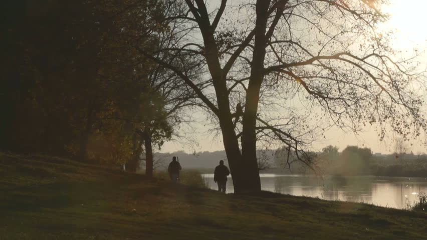 hunters with dog on the lake at sunset,  sunset on the oak grove on a lake, sunset on the riverbank, oak tree on the lake at sunset, sunset on the autumn river, Silhouettes of the hunters at sunset,
