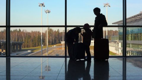 silhouettes of mother, son and daughter standing against window at airport