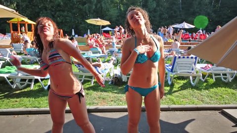 Two women shake their hair near open-air swimming pool with vacationers