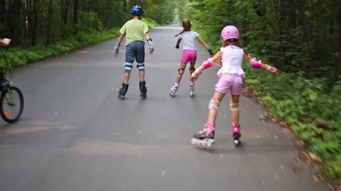 Back of three children riding on roller skates and woman riding bicycle
