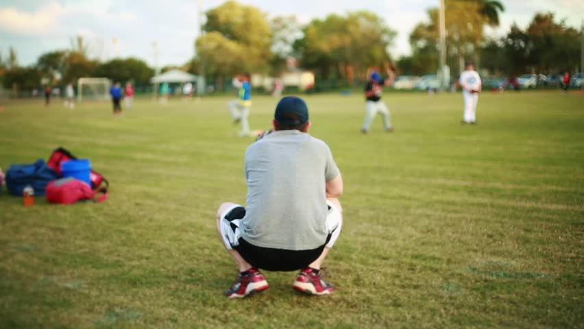Shot from behind of male adult throwing ball to a kid during a baseball practice at baseball field. Unrecognizable people on the shot