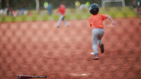 Shot of Unrecognizable Kid Running the bases at a Baseball Game. At the end of the shot you can see a game of soccer in the back.