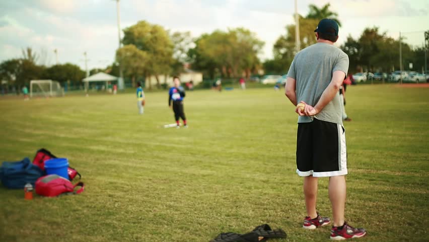 Shot from behind of Adult Male Pitching to a kid during a Baseball Practice at Baseball Field. Unrecognizable people on the shot