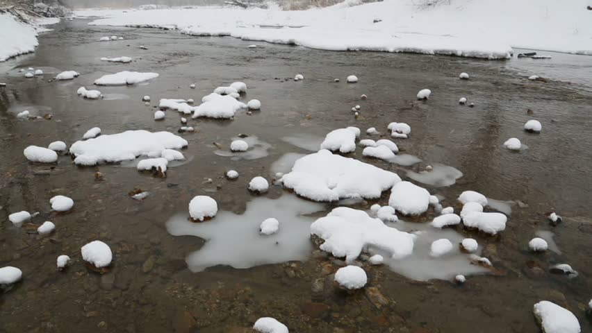 Winter landscape on the river with falling snow. The first days in March, Russia.