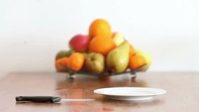 Shot of female hands cutting pear in kitchen surrounding, bowl of fruits in the background
