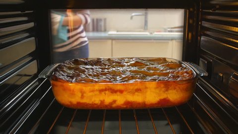 Woman opens door of oven and takes out dish of cooked lasagne. Shot on Sony FS700 at a frame rate of 25 fps