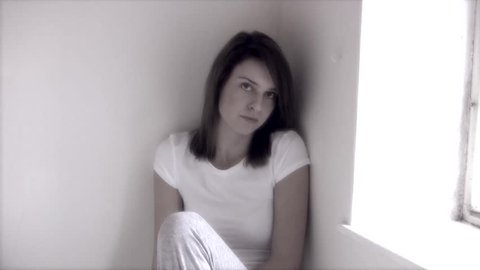 Depression, young woman aged 20 to 25 sitting in corner of white room looking depressed