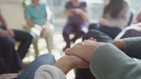 4K Couple holding hands for support during group therapy session. Focus on the hands.