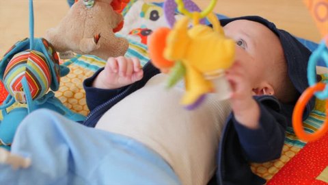 A newborn baby boy lying on his back playing with his toys
