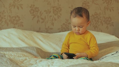 Young child watching mobile phone, sitting on bed