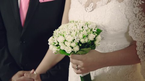 Interior shot at a wedding ceremony.The groom holds the bride's hands tightly while she is holding on the other hand the wedding bouquet.Couple at wedding groom holds bride's hand tight