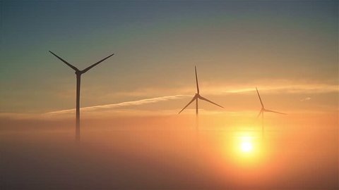 Wind turbines slowly spinning during a foggy, spring sunrise.