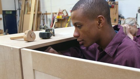 Two apprentices in carpentry workshop working on cabinet.Shot on Sony FS700 at a frame rate of 25fps