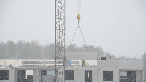 VILNIUS, LITHUANIA - JANUARY 21, 2014: Crane lift concrete block house part and builders workers on flat house roof in snow fall blizzard on January 21, 2014 in Vilnius, Lithuania. Static shot.