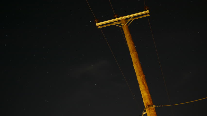 Old wooden electricity pole against dark sky with moving stars