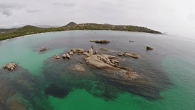 Flight over the sea with rocks and stones in water, Corsica, Santa Giulia beach. Aerial panoramic view.