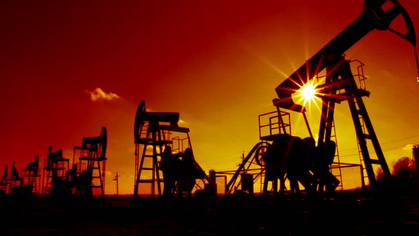 row of many working oil pumps silhouette against sun
