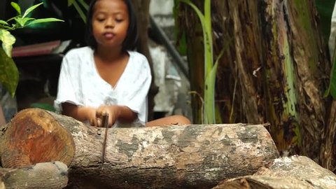 a girl saws a piece of fallen wood branch to be used as firewood