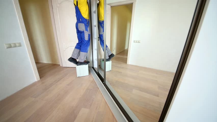 Young worker fixes side guide profile of sliding wardrobe.