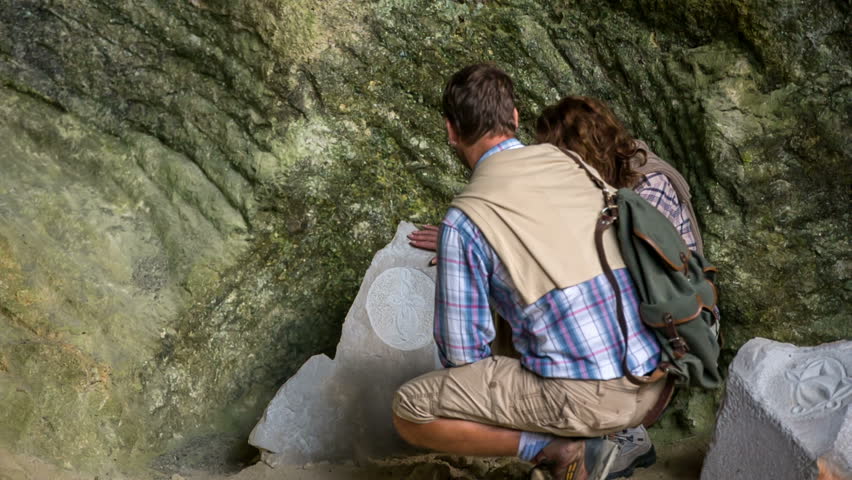 Couple admiring the art in the stone . Close up footage of a couple examine the stone in front of the nature camera and is imprest above the art.