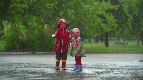 Two kids having fun under umbrella bouncing in the puddle