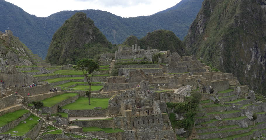 Mid shot of Machu Pichu with fog raising and tourists milling about.